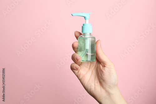 Woman holding antiseptic gel on pink background, closeup