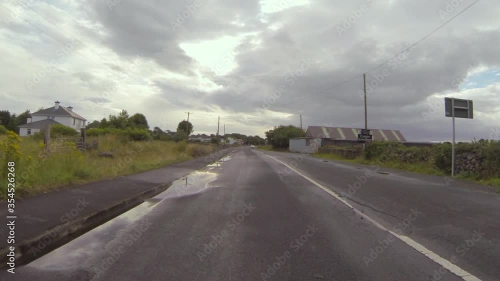 POV shot of wet road amidst trees and plants in town against sky - Galway, Ireland POV shot of wet road amidst trees and plants in town against sky - Galway, Ireland