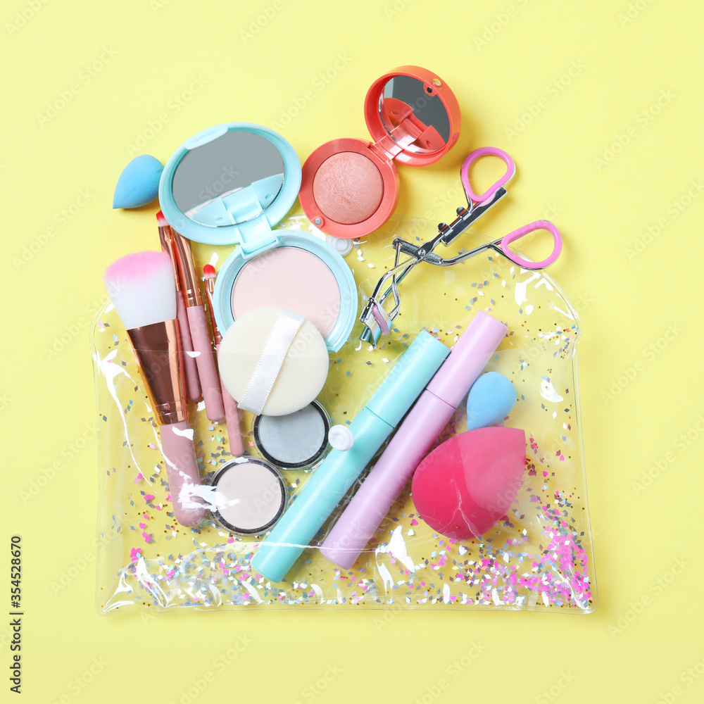 Naklejka premium Plastic cosmetic bag with makeup products and beauty accessories on yellow background, flat lay
