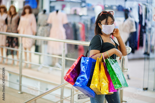 African american woman wearing face protective medical mask for protection from virus disease with shopping bags in mall during coronavirus pandemia.
