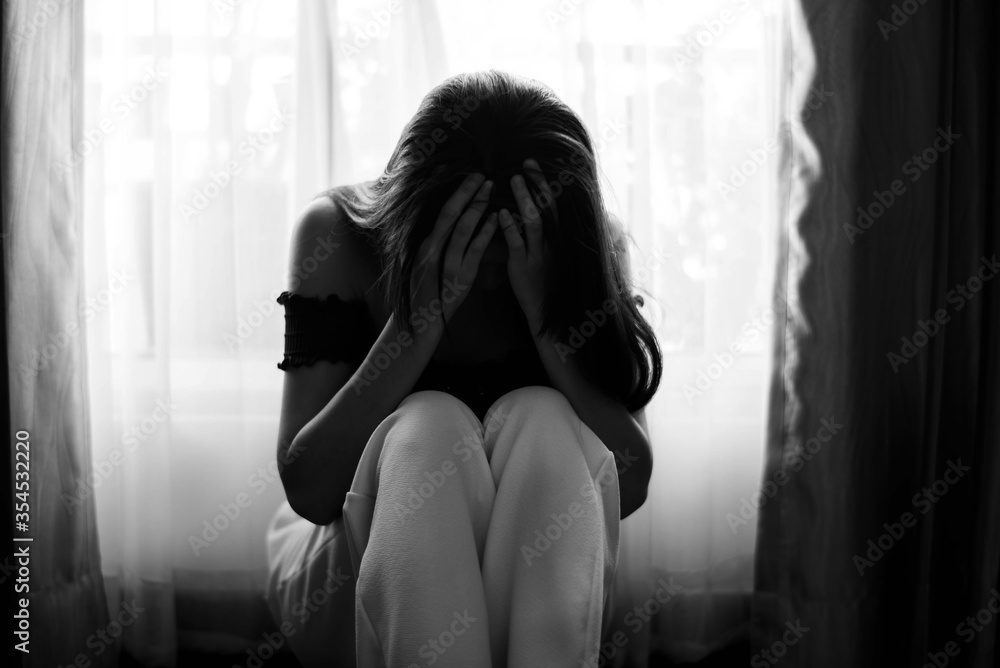 Sad and depressed young Female sitting on the floor in the living room looking outside the doors,sad mood,feel tired, lonely and unhappy concept. Selective focus.