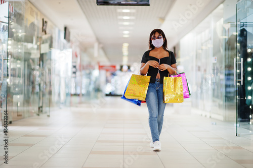 African american woman wearing face protective medical mask for protection from virus disease with shopping bags in mall during coronavirus pandemia.