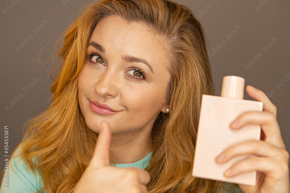 A young girl sniffs perfume. Beauty blogger is testing perfume. A young girl advises makeup.Isolated portrait of a girl with a pink perfume bottle in hands