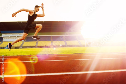 Young handsome athlete running at the stadium at sunset 