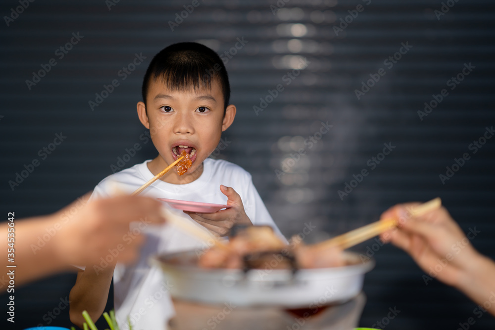 Kid eating grilled meat on night background, grilled pork meat and seafood in chopsticks on hot steam smoke water from hot pan for cooking in party, roasted meat on night background for people eating Kid eating grilled meat on night background, grilled pork meat and seafood in chopsticks on hot steam smoke water from hot pan for cooking in party, roasted meat on night background for people eating