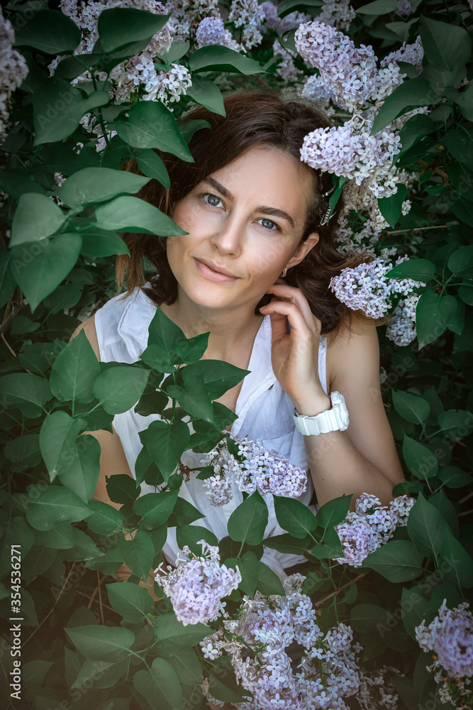 Pretty fresh darkhaired young woman wearing summer floral dress feminine posing against the backdrop of a blossoming lilac tree .Concept of summer holidays at village and live style. Pretty fresh darkhaired young woman wearing summer floral dress feminine posing against the backdrop of a blossoming lilac tree .Concept of summer holidays at village and live style.