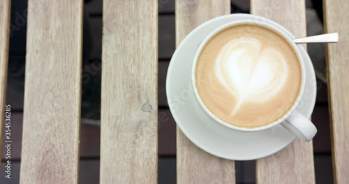 Overhead shot of cup of cappuccino being put down on wooden table