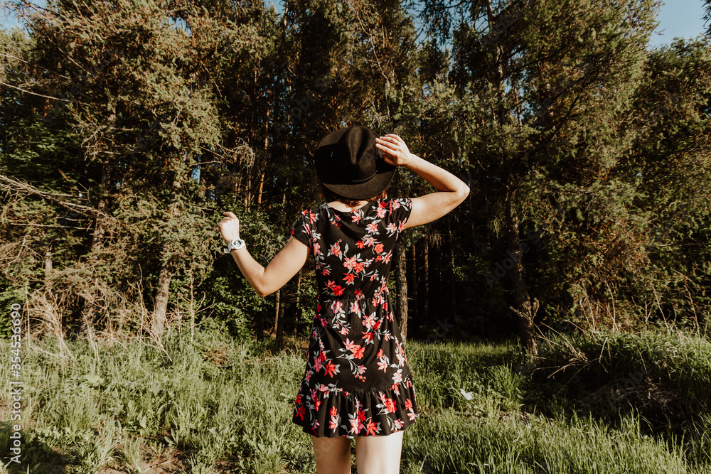 lifestyle photo of young beautiful darkhaired woman in a black dress stands with his back to the camera on a background of green forest and field. Girl calling with herself on a journey lifestyle photo of young beautiful darkhaired woman in a black dress stands with his back to the camera on a background of green forest and field. Girl calling with herself on a journey