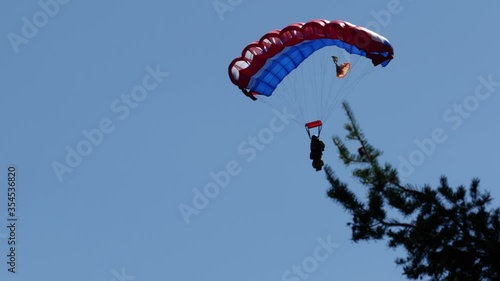 A smoke jumper is seen parachuting with a group of other smoke jumpers falling into the sage brush. photo