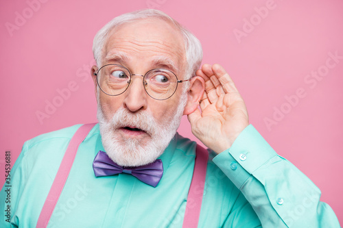 Closeup photo of attractive grandpa hand near ear listen rumors focused chatterbox bad person wear specs mint shirt suspenders violet bow tie isolated pink pastel color background photo