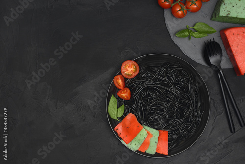 Black pasta. Black spaghetti with cheese  tomato and basil in black plate over black background with copy space. 