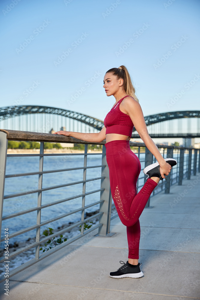 Fit in the city, young woman doing gymnastics and stretching exercises on the river early in the morning after sunrise Fit in the city, young woman doing gymnastics and stretching exercises on the river early in the morning after sunrise