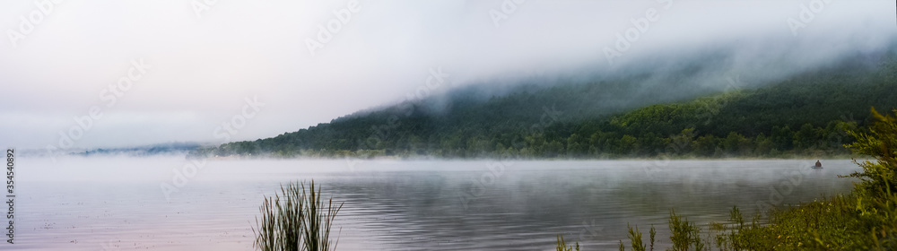 fisherman in a boat and foggy landscape overlooking the river