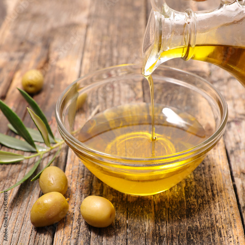 olive oil pouring in bowl with green olive and herb