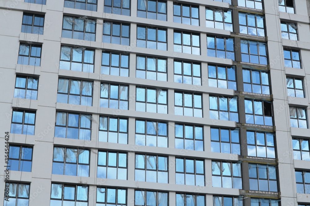 Windows of new buildings with the remains of the packaging film on the glass. The sky is reflected in the windows of a building under construction. Abstract urbanistic background. Windows of new buildings with the remains of the packaging film on the glass. The sky is reflected in the windows of a building under construction. Abstract urbanistic background.
