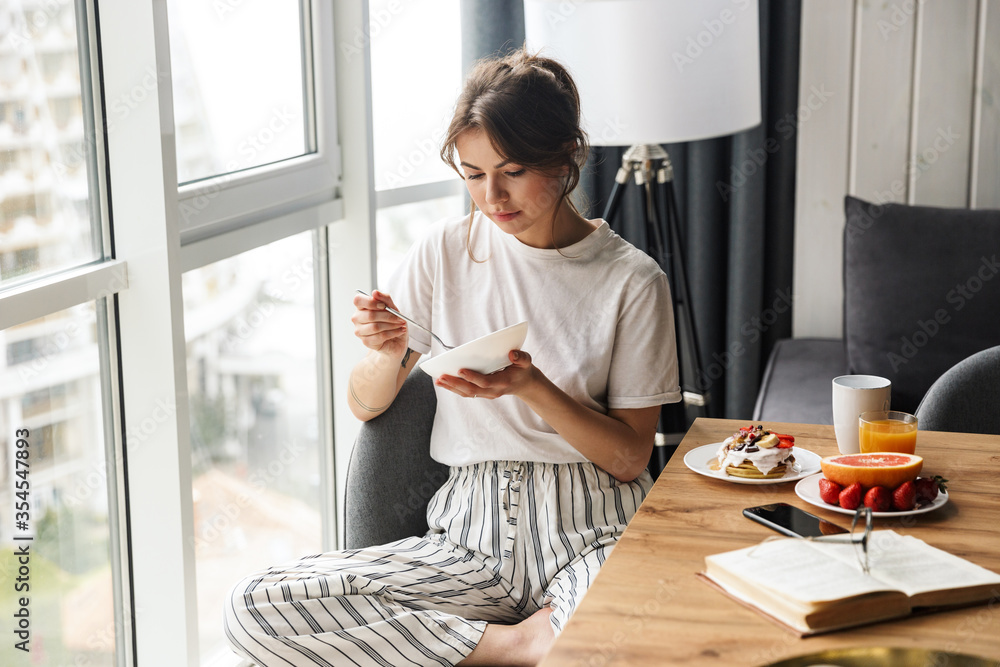 Photo of young cute woman having breakfast while sitting at table Photo of young cute woman having breakfast while sitting at table