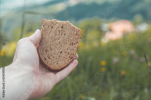 Making lunch on hiking holiday. Close up of piece of bread, beautiful idyllic landscape in the blurry background.