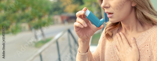 Closeup view of woman using asthma inhaler outdoors, space for text. Banner design photo