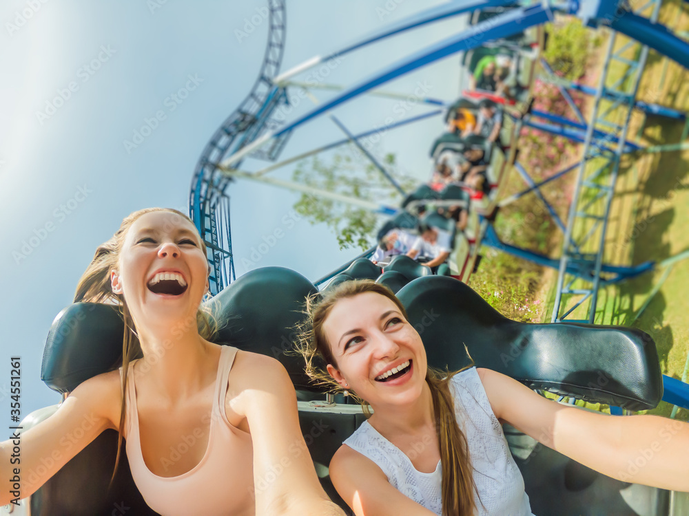Two happy girls having fun on rollercoaster - obrazy, fototapety, plakaty 