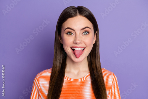 Closeup photo of pretty lady sticking tongue out mouth teasing friends boyfriend naughty behavior wear casual orange striped t-shirt isolated pastel purple color background