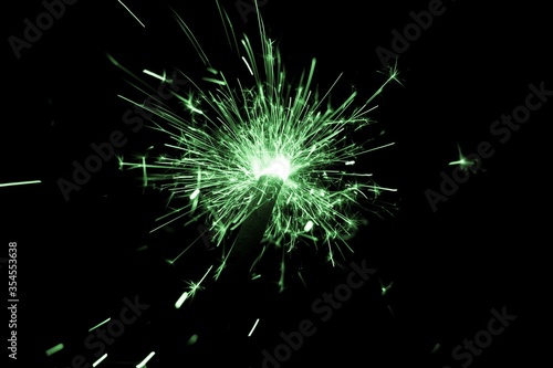 Green sparkler countdown on fire with spread of glitter sparks. Luxury entertainment at e.g. New Years Eve  Independence Day or birthday party celebration. Glowing light spark on dark background