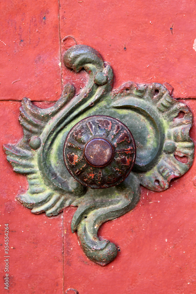 Close-up of an ancient, often used copper metal detail on red door. Green vedigris contrasting with red paint. Part of door to cistercian monastery Porta Coeli in Predklasteri, Czech Republic, Europe. Close-up of an ancient, often used copper metal detail on red door. Green vedigris contrasting with red paint. Part of door to cistercian monastery Porta Coeli in Predklasteri, Czech Republic, Europe.