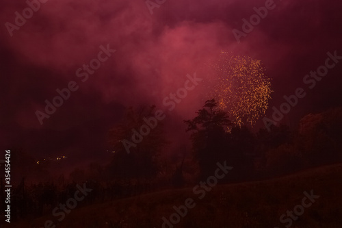 Orange fireworks over trees silhouette and against the backdrop of the night sky, Vittorio Veneto, Italy. Concept: religious recurrence, celebration, colors, tradition