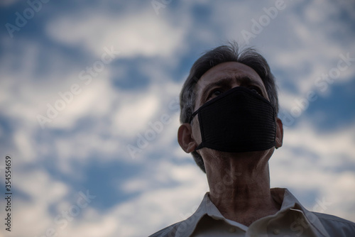 Low angle view of Indian old man with corona virus protective mask below the blue cloudy sky. Home isolation and Indian lifestyle © abir