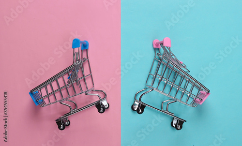 Two mini supermarket trolleys on blue pink pastel background. Shopping concept. Top view. Minimalism