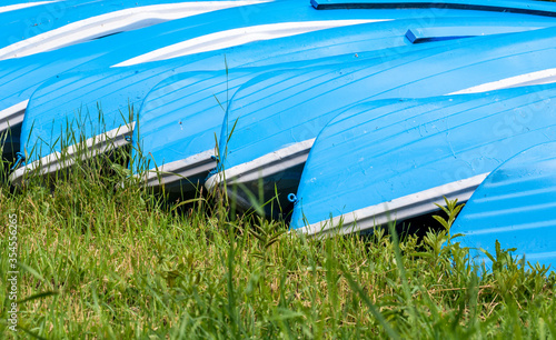 Blue fishing boats stacked on green grass. Pile of blue boats