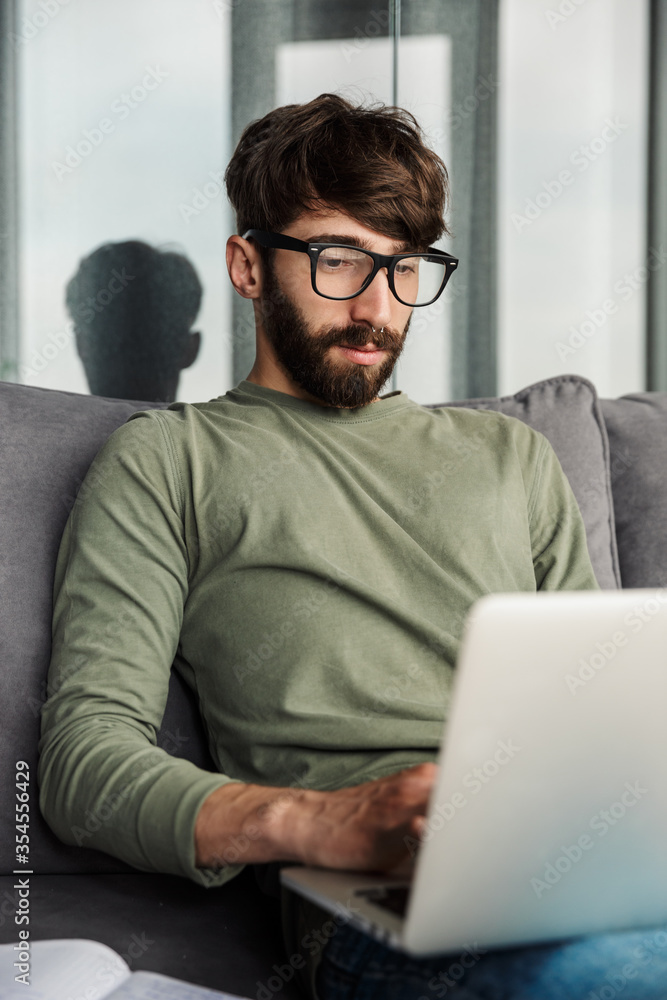 Image of focused bearded man working with laptop while sitting on sofa Image of focused bearded man working with laptop while sitting on sofa