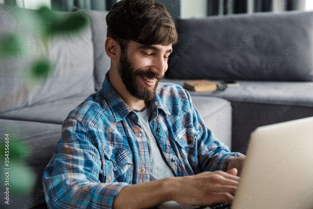 Image of laughing man working with notebook while sitting on floor Image of laughing man working with notebook while sitting on floor