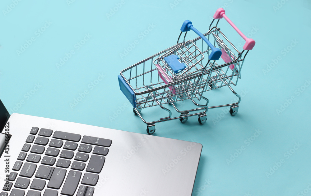 Online shopping. Laptop with supermarket trolleys on a blue pastel background