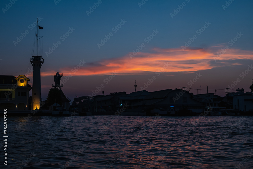 Sunrise or sunset view of Chao Phraya River , Bangkok, Thailand . Shows water transport. reflective of the sun. Image contain certain grain or noise and soft focus.