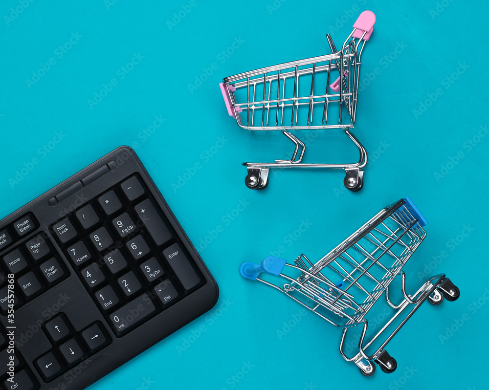 Online shopping. PC keyboard with supermarket trolleys on blue background. Top view. Flat lay