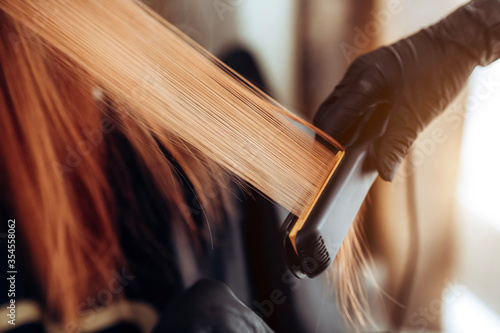Print op canvas Close-up of a hairdresser straightening long brown hair with hair irons