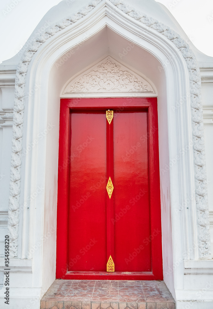 Red wooden temple doors With a white concrete arch Is a unique temple in Thailand.