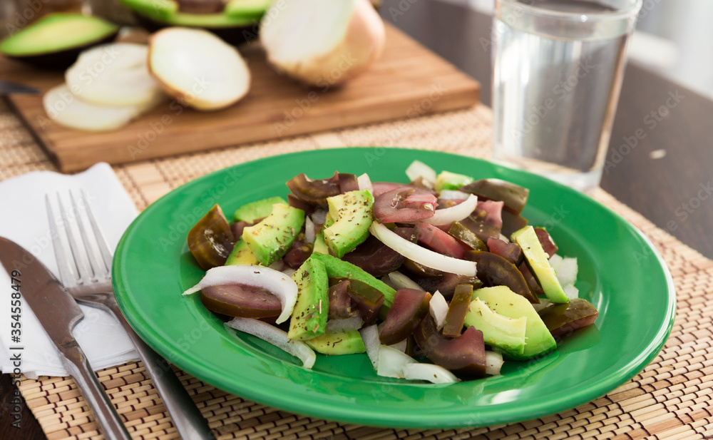salad of black tomatoes, avocado and onions on green plate