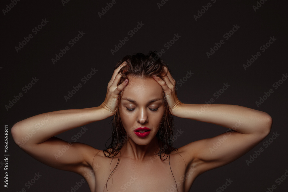 Fototapeta premium Lovely. Portrait of beautiful stylish woman isolated on dark studio background. Caucasian model with red lipstick, wet hair and shiny skin, bright make up. Beauty, fashion, emotions concept.