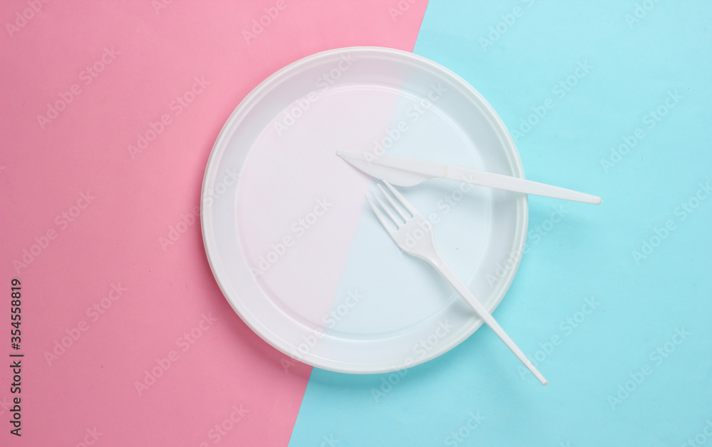 Plastic plate with fork and knife on pink blue background. Picnic. Plastic pollution. Top view Plastic plate with fork and knife on pink blue background. Picnic. Plastic pollution. Top view