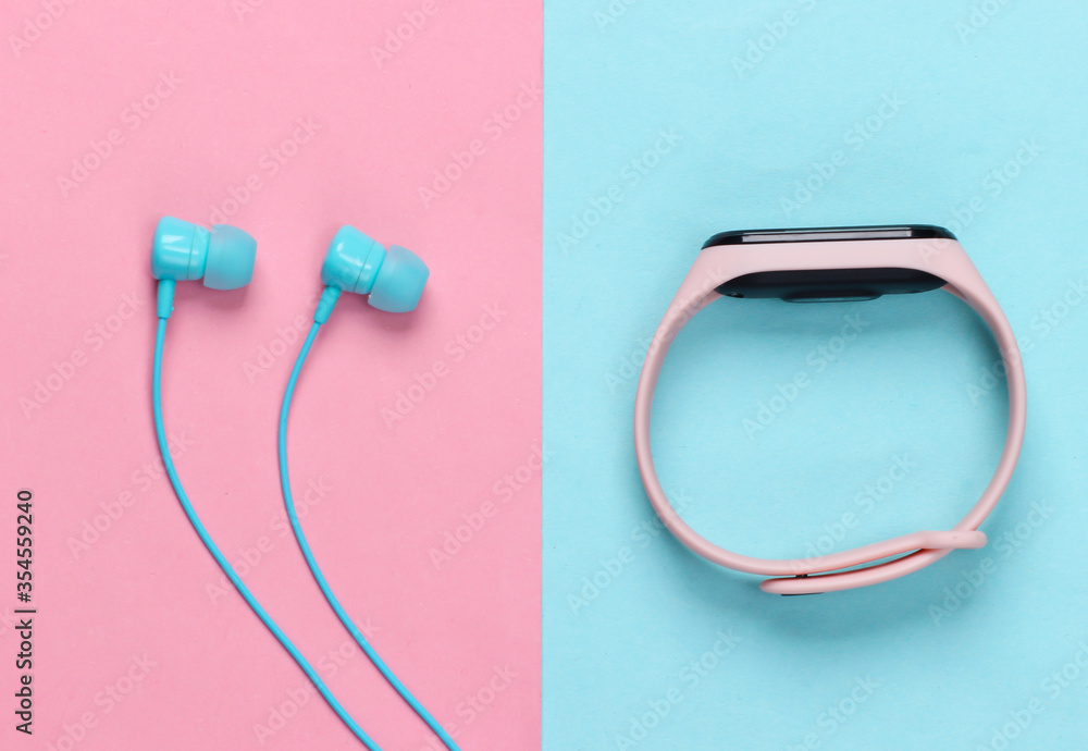 Earphones with smart bracelet on pink blue pastel background. Modern gadgets. Top view Earphones with smart bracelet on pink blue pastel background. Modern gadgets. Top view