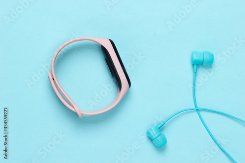 Earphones with smart bracelet on blue pastel background. Modern gadgets. Top view