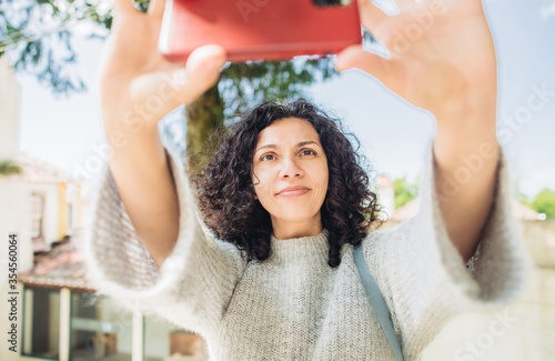 Young curly brunette woman talking a selfie or having a video call from the outside. Concept of the end of the quarantine and the beginning of travelings  photo