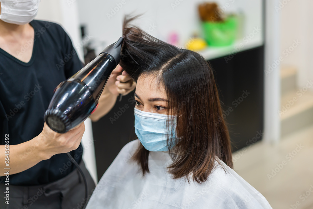 hairdresser using hair dryer and comb to the hair of woman, people must be wering medical mask to protection coronavirus (covid-19) pandemic. new normal concepts hairdresser using hair dryer and comb to the hair of woman, people must be wering medical mask to protection coronavirus (covid-19) pandemic. new normal concepts