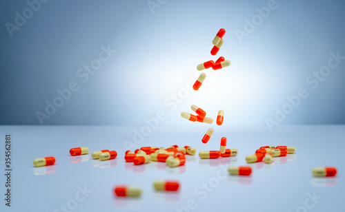 Yellow-orange capsules pill falling down on white table. Pharmaceutical industry. Tranexamic acid capsule pills for treatment heavy menstrual bleeding (Menorrhagia). Pharmaceutical manufacturing. photo