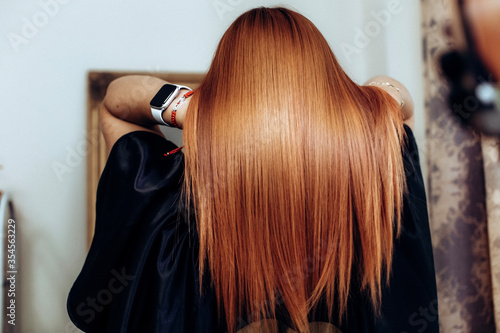 Professional hairdresser shooting straight clients redhead hair after hair care beauty procedures. Back view.