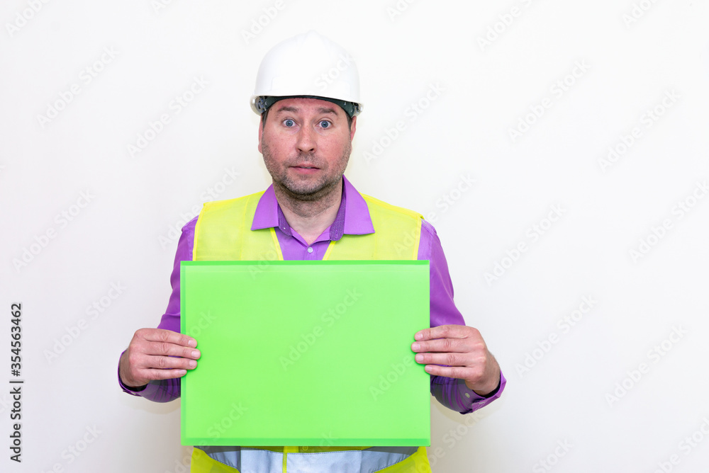 Portrait of curious surprised architect in a construction helmet holding a folder, free place mock up banner advertisement.Studio shoot. Portrait of curious surprised architect in a construction helmet holding a folder, free place mock up banner advertisement.Studio shoot.