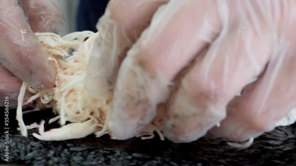 Man in gloves is making a sushi roll with black rice using bamboo mat. Closeup view of process of cooking sushi Man in gloves is making a sushi roll with black rice using bamboo mat. Closeup view of process of cooking sushi
