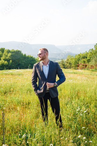 Young groom in a wedding suit on a background of a landscape of mountains. © Ekaterina Pichukova