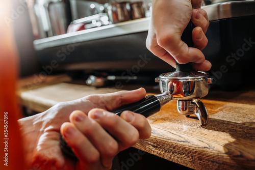 Barista making coffee and holding a portafilter in hands and pressing coffee. Close-up